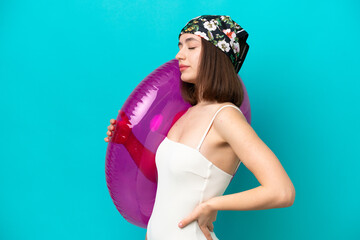 Young Ukrainian woman holding air mattress isolated on blue background suffering from backache for having made an effort