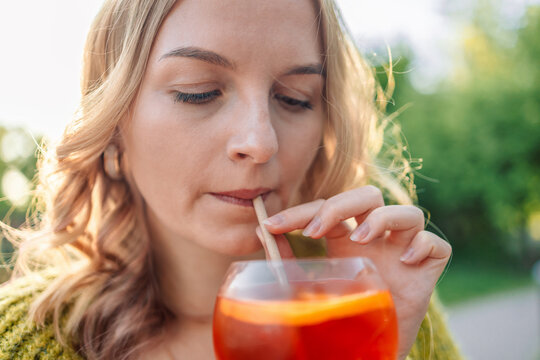 Closeup image of happy European 30s blonde woman having fun in cafe and drinking fruit cocktails with pleasure, outfit chilling in restaurant or street cafe