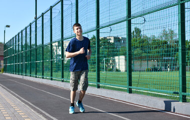 a teenage boy trains on a sports ground outdoors, he runs, does physical exercises, a healthy lifestyle, a bright sunny day in summer