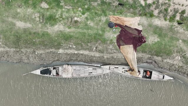 Fishermen pulling nets from boats on the banks of the river - Top aerial view drone video footage