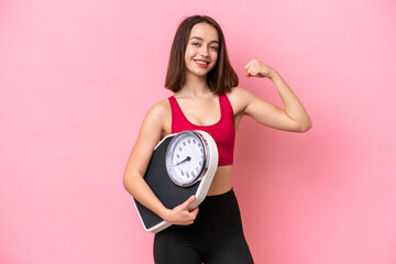 Young Ukrainian woman isolated on pink background holding a weighing machine and doing strong gesture