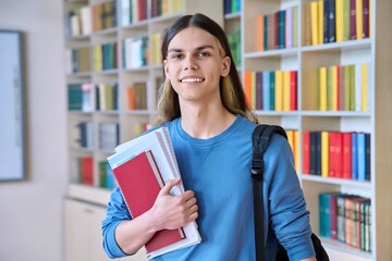 Portrait of a student guy with textbooks looking at camera in college library
