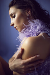 portrait woman in an evening purple dress with feathers stands in the background in the studio.