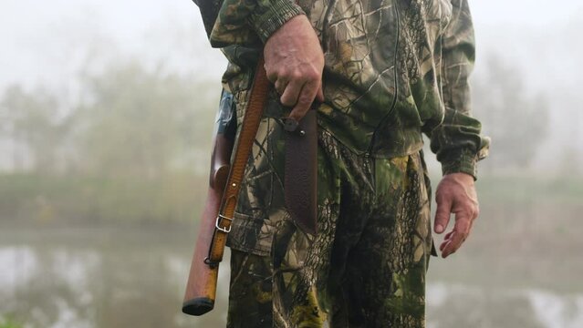 A hunter with a weapon slowly gets out of his knife near a misty lake