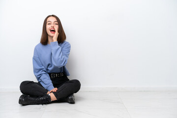 Young Ukrainian woman sitting on the floor isolated on white background shouting with mouth wide open