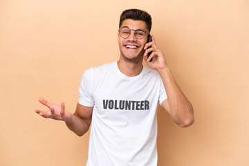Fototapeta premium Young volunteer caucasian man isolated on beige background keeping a conversation with the mobile phone with someone