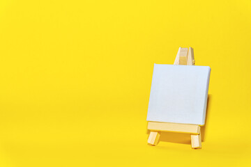 Drawing equipment, wooden easel with blank canvas on a yellow background. Background for designers...