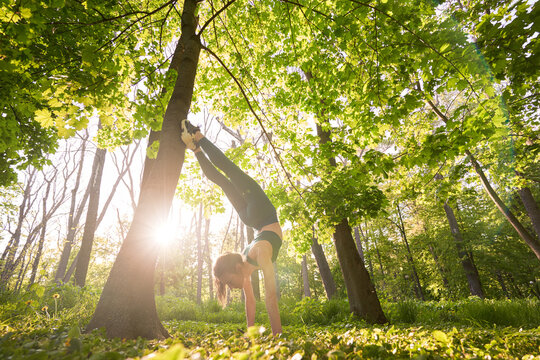 Athletic slim woman exercising balance in handstand in nature