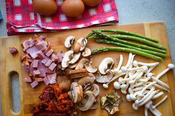 Mushrooms, asparagus and bacon cut on a wooden board.