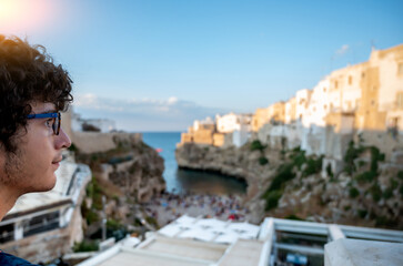Polignano a mare, Puglia, Italy. August 2021. A young man with curly hair and glasses admires the...