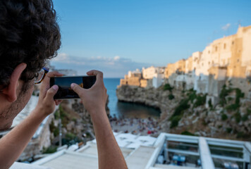 Polignano a mare, Puglia, Italy. August 2021. A young man with curly hair and glasses admires the...