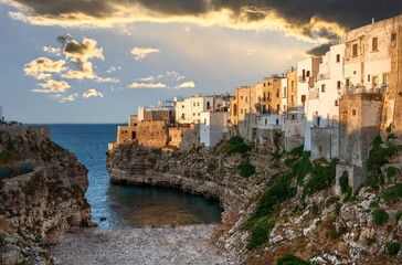 Fototapeta na wymiar Polignano a mare, Puglia, Italy. August 2021. Amazing aerial view of Cala Monachile: the picturesque and fascinating beach of the historic center. At sunset, the golden hour, people enjoy the place.