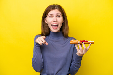 Young English woman holding sashimi isolated on yellow background surprised and pointing front