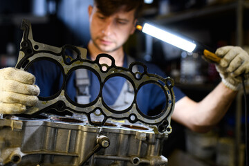 Blurred serviceman in gloves holding lamp and pad of damaged engine in garage 