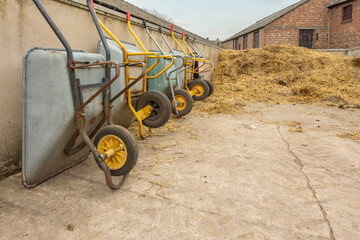 wheelbarrows stacked in a line against a wall in a farm straw pile