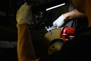 Partial view of auto service worker holding lamp and caliper near car disc brake 