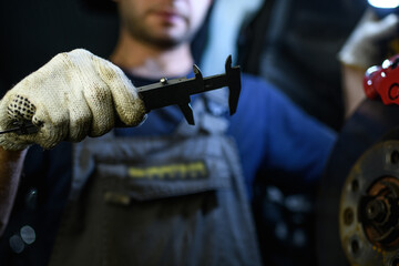 Partial view of auto mechanic in glove holding caliper near blurred disc brake in garage 