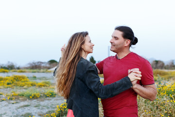 Portrait of lovely middle-aged couple looking on each other and hugging while dancing on grass in summer park.