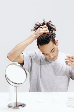 portrait of a man applying cream on the face and looking in the mirror cosmetology light background