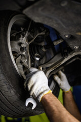 Partial view of mechanic in gloves holding wrench near car wheel in service station 