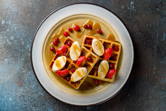 waffles with fresh strawberries, bananas and powdered sugar on blue stone table