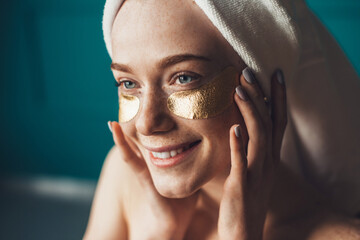 Freckled woman applying golden patches under eyes touching face with hands. Natural beauty. Skin care. Rejuvenation treatment. Eye care.