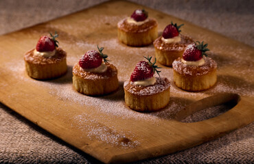 Muffins on a wooden board decorated with cream and strawberries and with powdered sugar