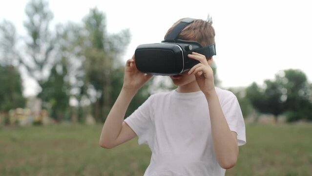 Happy boy in virtual reality glasses plays video games outdoors.