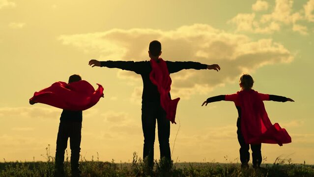 Happy kids playing superhero against sky. Boy plays superhero in red cape, childhood dream. Little hero in red cloak looks at sunset. Brave victorious child in raincoat plays, nature. Childhood dreams