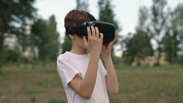 Happy boy in virtual reality glasses plays video games outdoors.