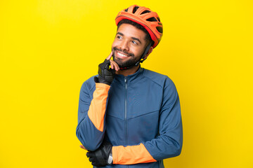 Young cyclist Brazilian man isolated on yellow background thinking an idea while looking up