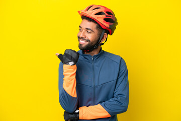 Young cyclist Brazilian man isolated on yellow background pointing to the side to present a product