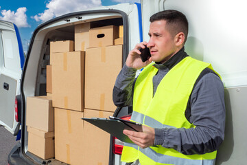 courier delivery. Courier is talking on phone. Delivery man is calling someone. Courier next to open minivan. Delivery service worker calls customer. Express minivan with lots of boxes.