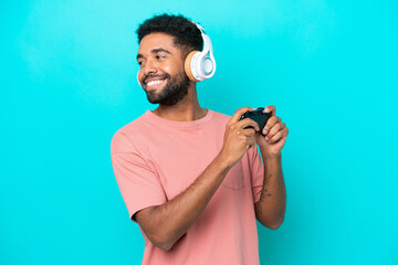 Young brazilian man playing with a video game controller isolated on blue background laughing in...