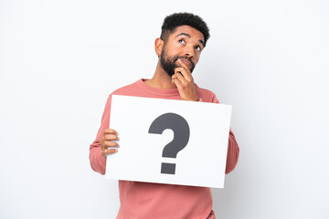 Young Brazilian man isolated on white background holding a placard with question mark symbol and...