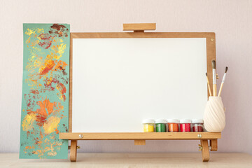 Blank white paper for painting on wooden easel on table at home studio - obrazy, fototapety, plakaty