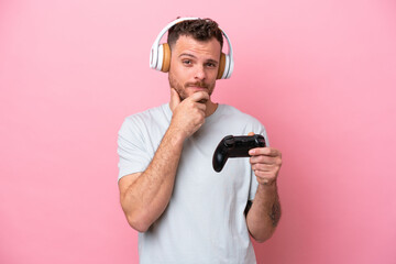 Fototapeta na wymiar Young Brazilian man playing with video game controller isolated on pink background thinking
