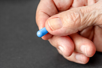 Old wrinkled hand holding a blue pill close up. Background with copy space.