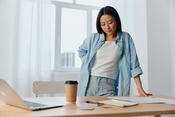 Concentrated thoughtful young Asian cute female businesswoman deals with documents reclines on table in light office interior. Employee work at home. Lady corporation leader concept. Copy space Offer