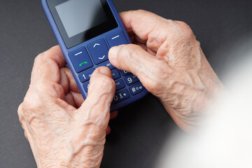 Old wrinkled hands holding a push-button mobile phone with big buttons. Elderly using cell phone...