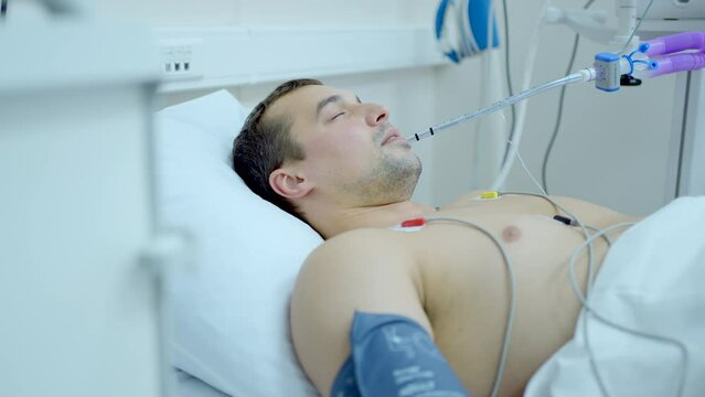 Caucasian man coming out of the coma at the hospital room. Action. Sick man in hospital bed, patient with a tube in his mouth.