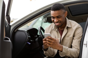 Happy smiling man typing a message on the phone while sitting in the car.