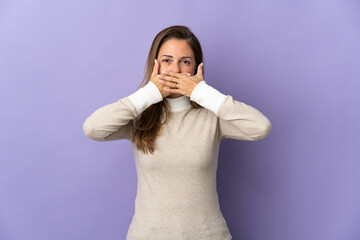 Middle age Brazilian woman isolated on purple background covering mouth with hands