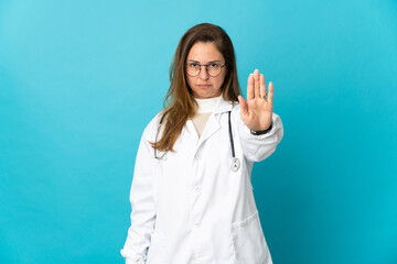 Middle age Brazilian doctor woman isolated on blue background making stop gesture