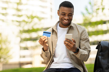 African young man shopping online with credit card using smartphone outdoors