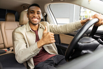 Young african american man smiling while driving a car showing thumbs up recommending something good. © Home-stock
