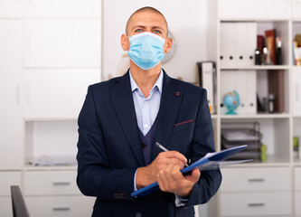 Portrait of young man manager in medical mask standing in modern office