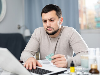 Man with pills in his hands is looking for diagnosis on the Internet using a laptop