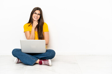 Young woman with a laptop sitting on the floor with glasses and smiling