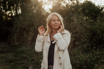 A beautiful adult woman with blond hair and a light raincoat smiles